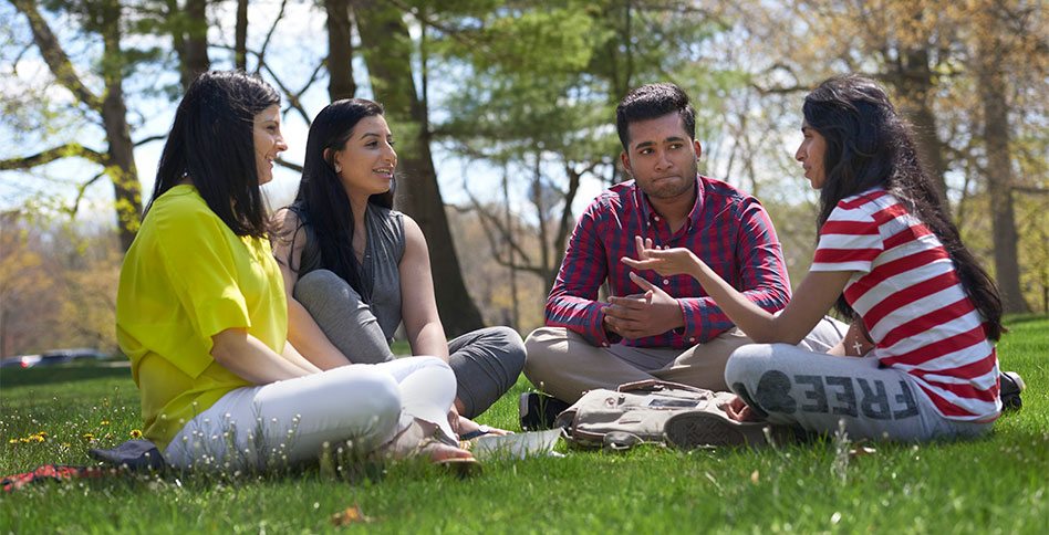 NYIT students sitting and  conversing in a grassy field
