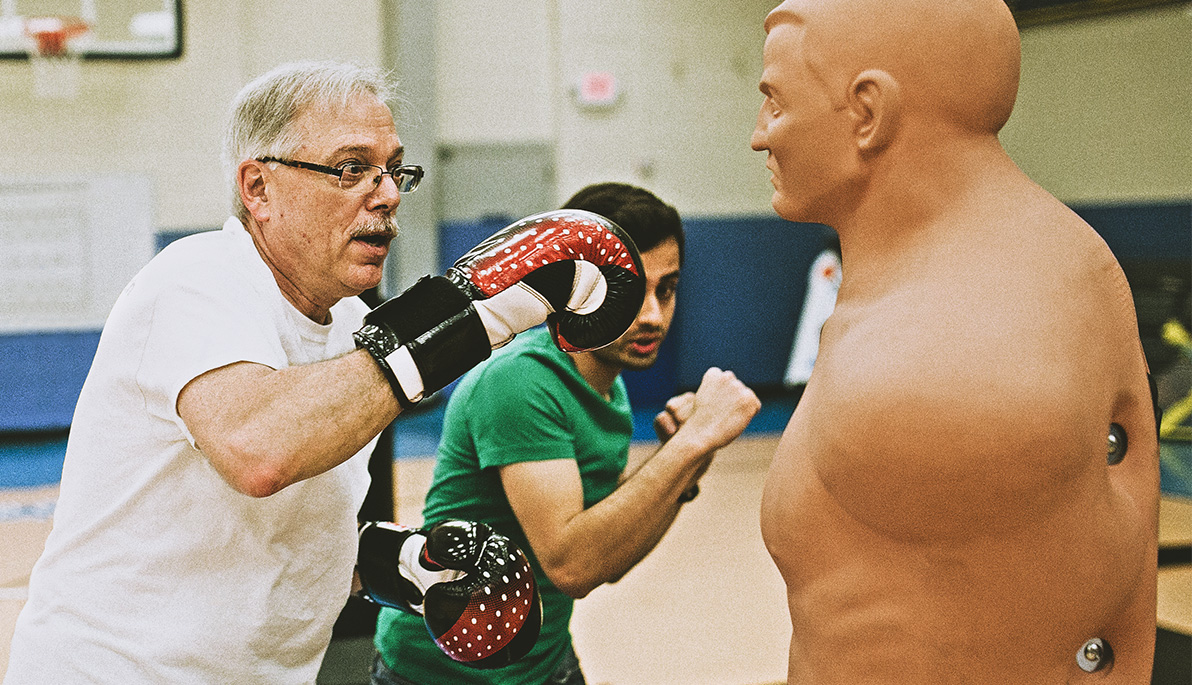 A participant in Rock Steady Boxing spars against a dummy as a student volunteer demonstrates technique.