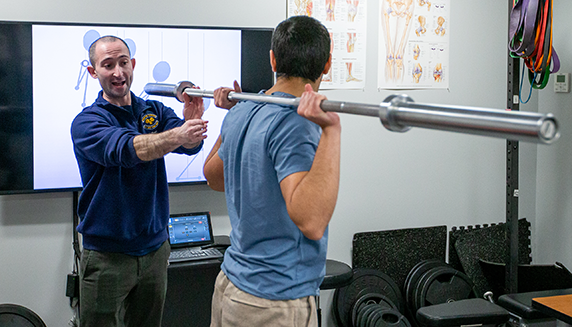 Instructor teaching student using a barbell