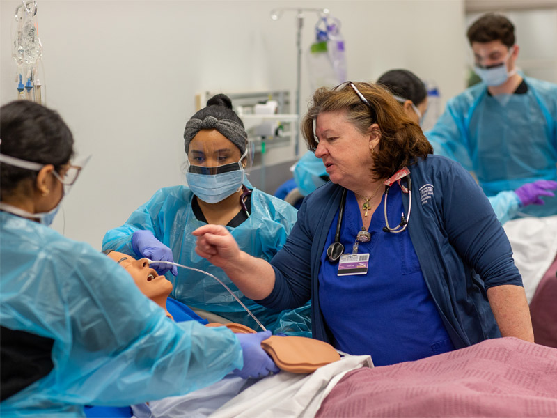 Student in full protective gear working in a simulation lab with an instructor. 