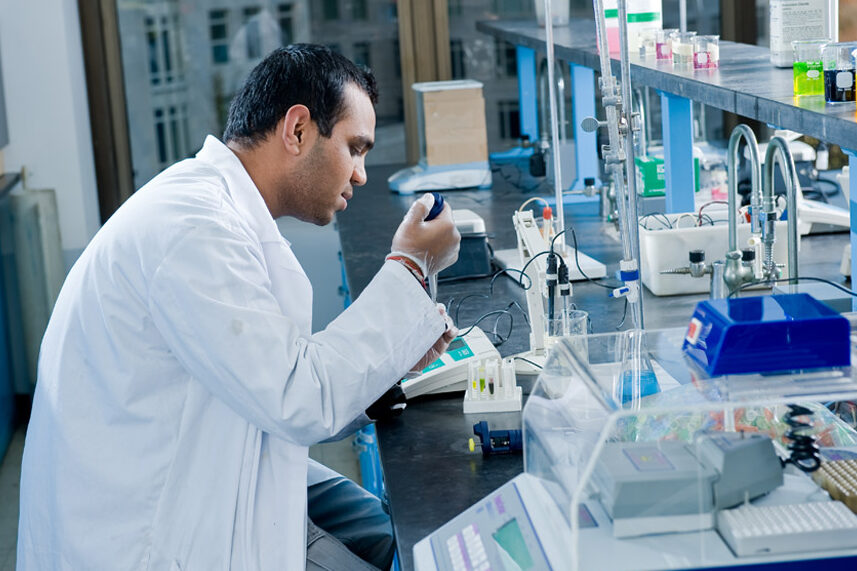 A student in a lab coat studies samples in a research laboratory at New York Tech.