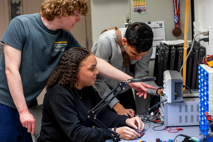 Three students in a lab classroom working with electrical equipment.