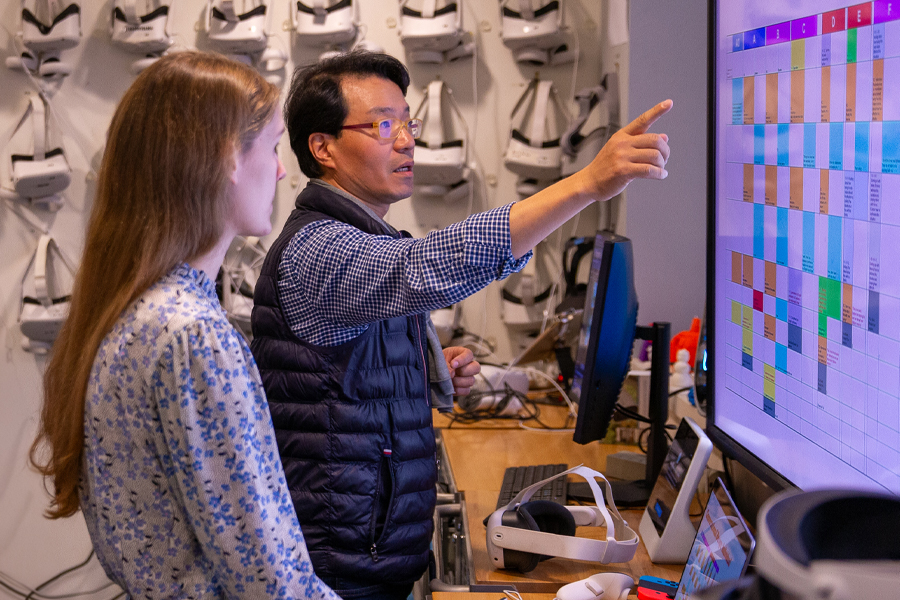 An instructor and a student working in a lab in front of equipment and a large screen. 