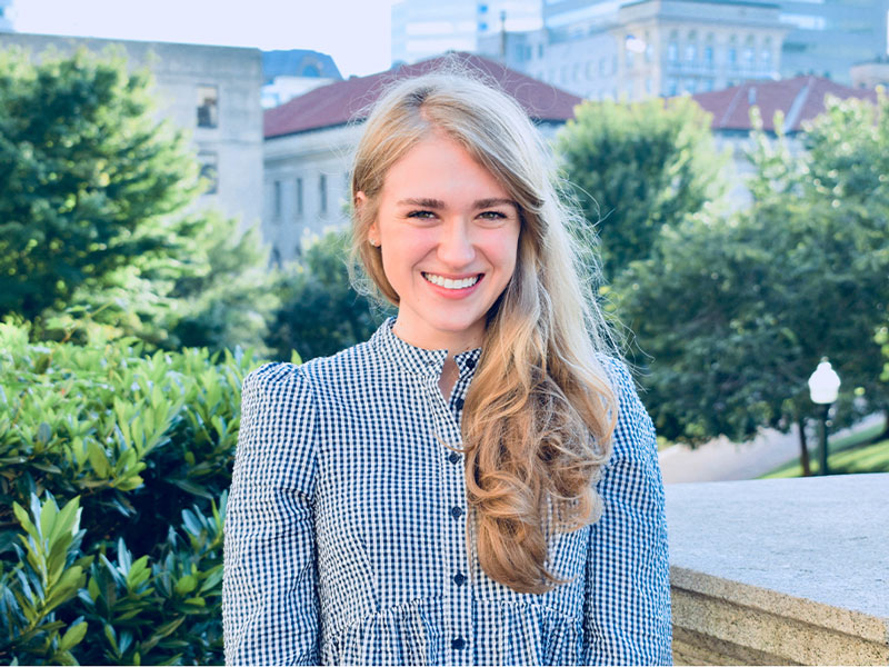 New York Tech aluma Brooke Danielsson, Ph.D. (B.S. ’16), stands outdoors in front of trees and buildings.