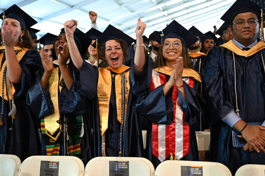 Group of students in caps and gowns cheering in a tent.