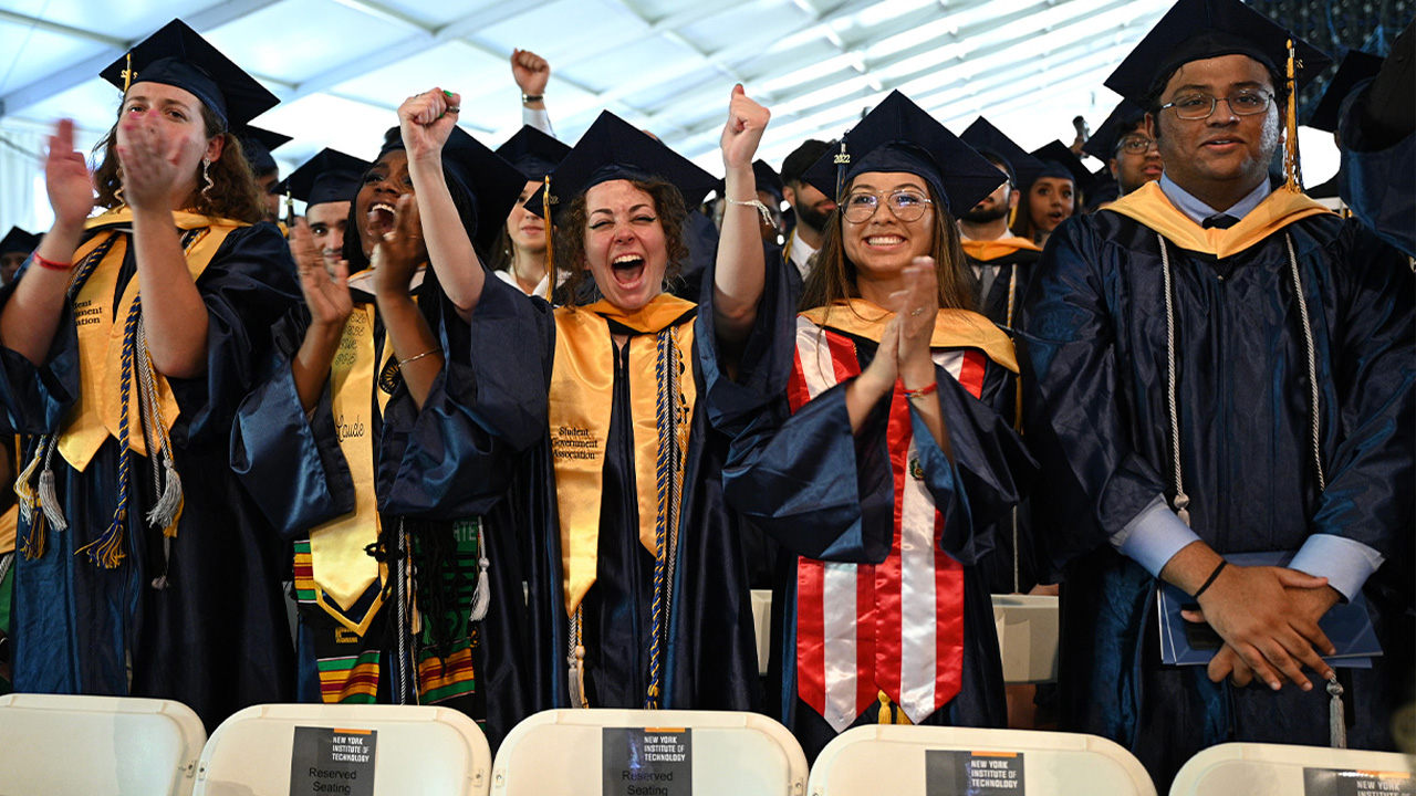 Group of students in caps and gowns cheering in a tent.