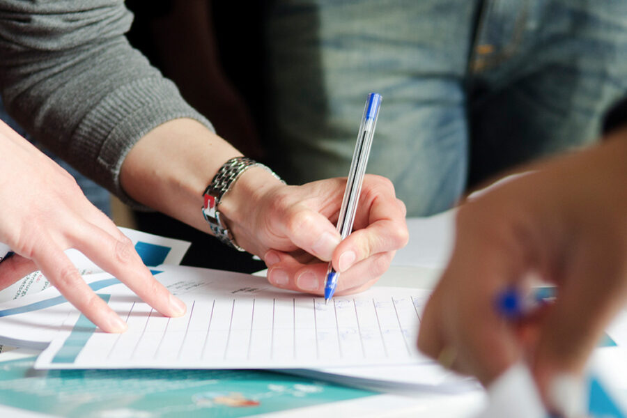 Diverse hands at a table signing up for a list or petition.