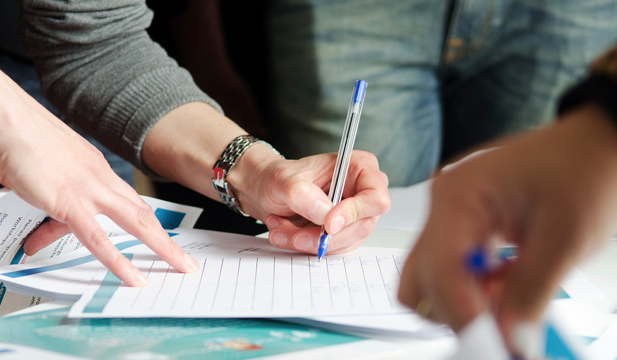 Diverse hands at a table signing up for a list or petition.