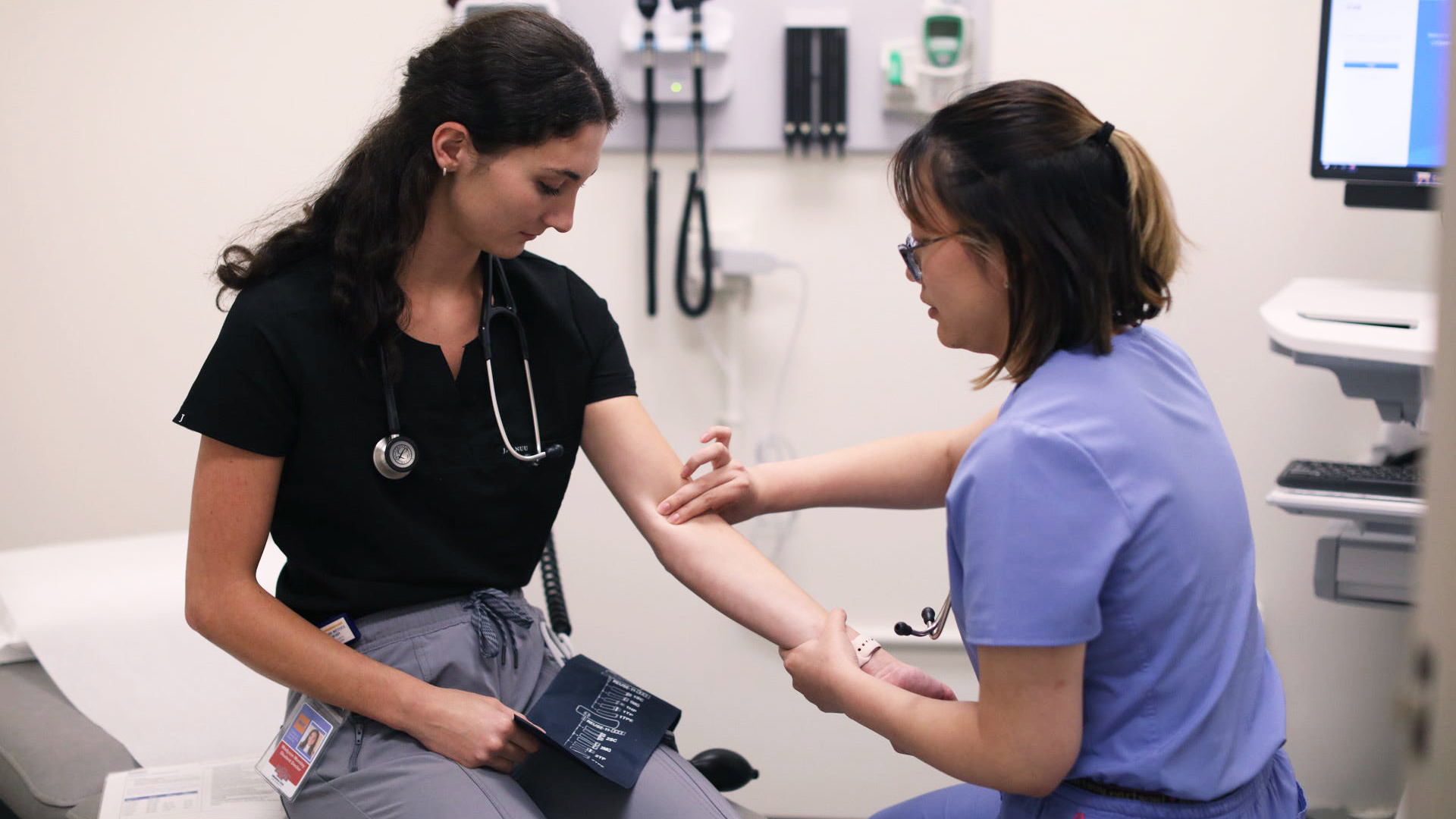 An NYITCOM-Arkansas student practices checking a patient's pulse by placing two fingers on another student's elbow.