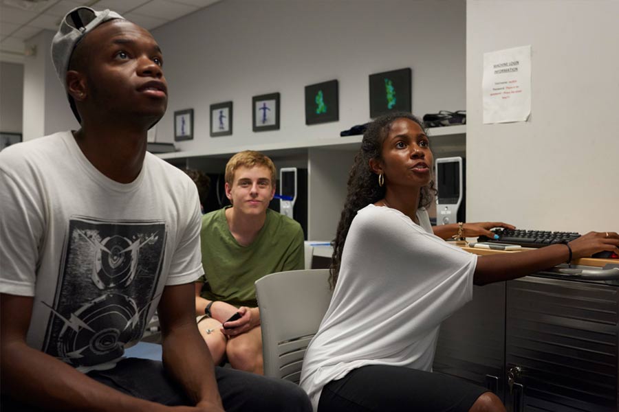 Instructor teaching a class of a computer. While two students observe.