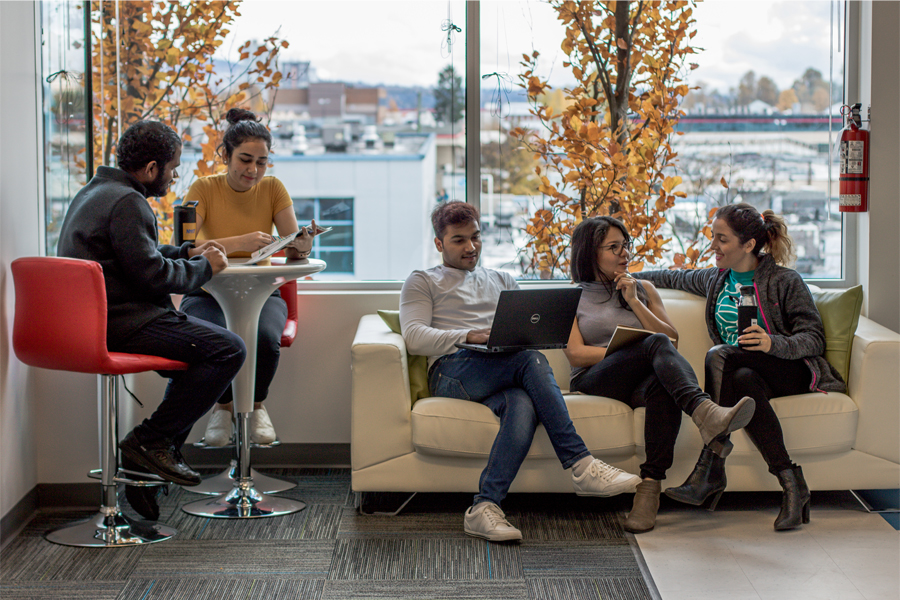 Two groups of students seat a table and couch in a study area. 