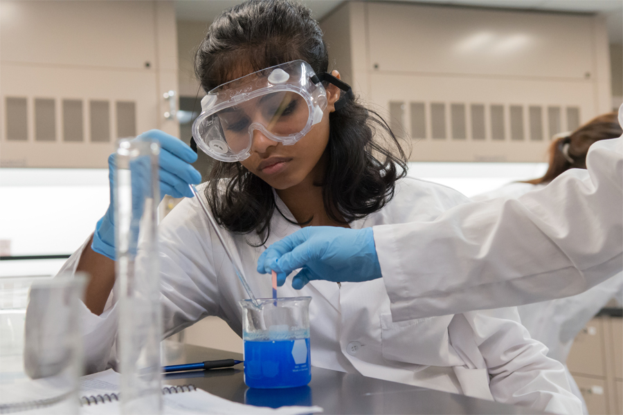 An international student wearing safety glasses drops a substance into a beaker while conducting an experiment in a New York Tech laboratory.