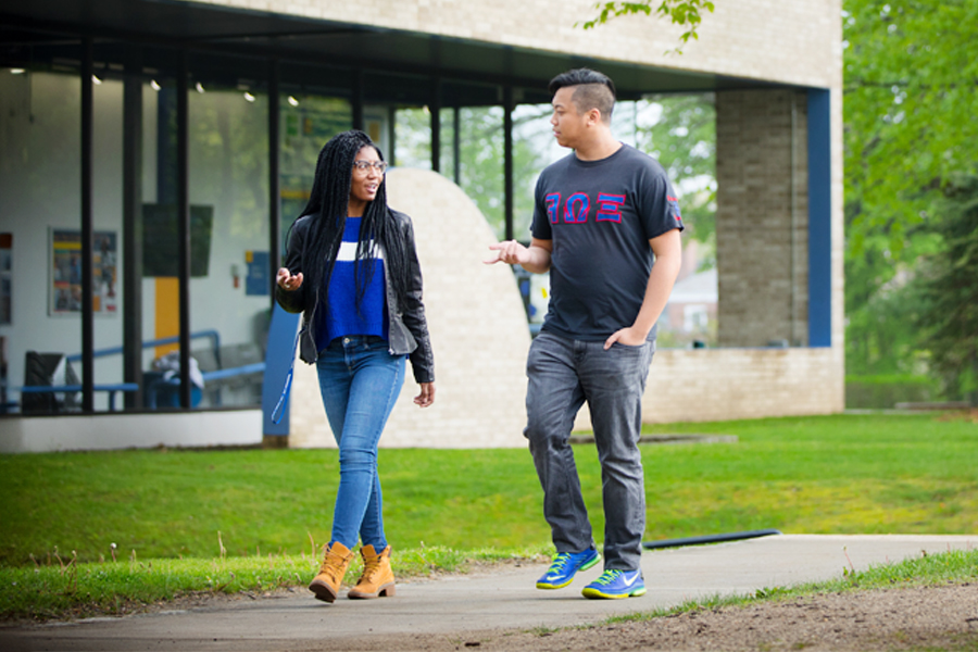 Two New York Tech transfer students walk along an outdoor path on the Old Westbury Campus.