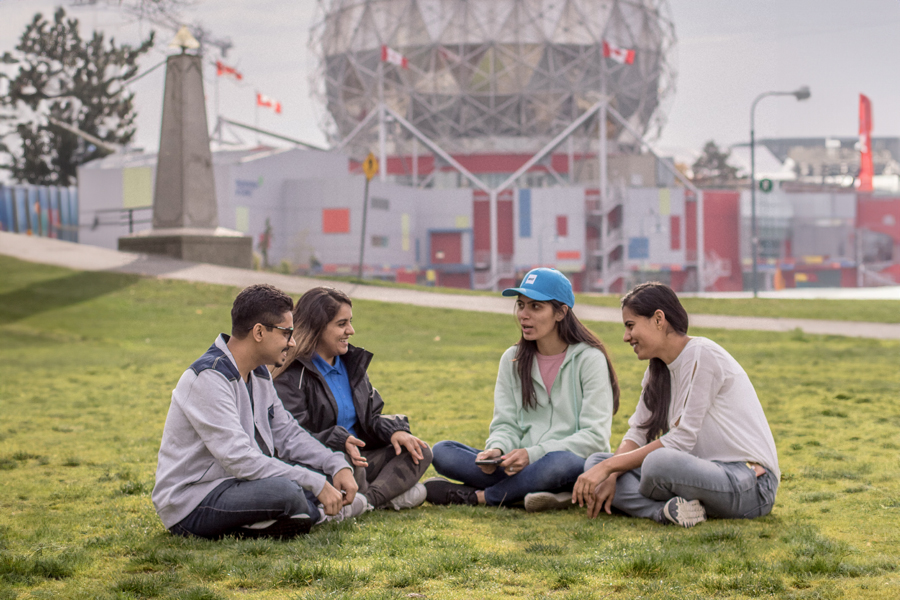 A group of four students sit in a semicircle on the grass near New York Tech's Vancouver campus.