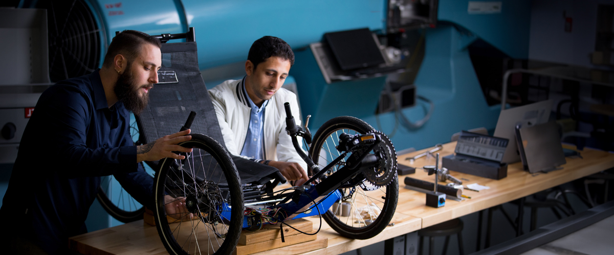 Two graduate students work on wheels for a device.