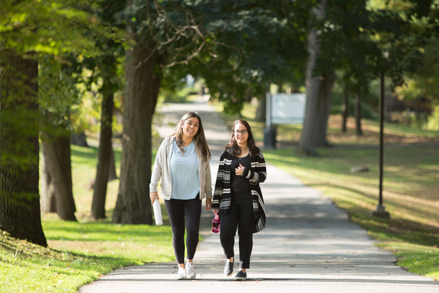 Two students walk along a tree-shaded path outdoors on New York Tech's Old Westbury Campus.