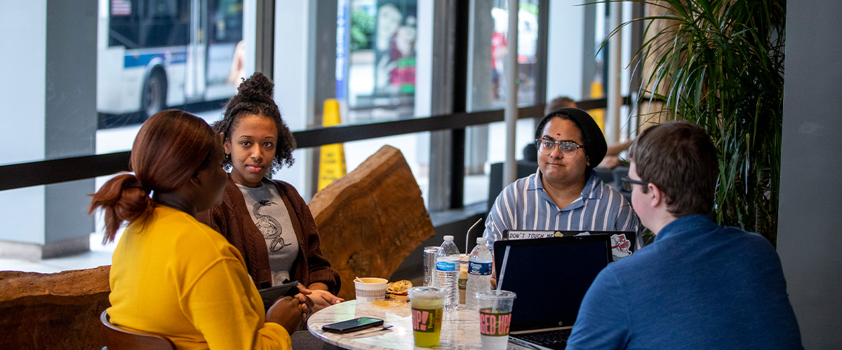 Students sitting at a round table with food and laptops.