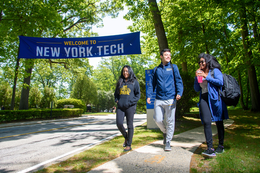 Three students walk around New York Tech's Long Island with a welcome banner above them.