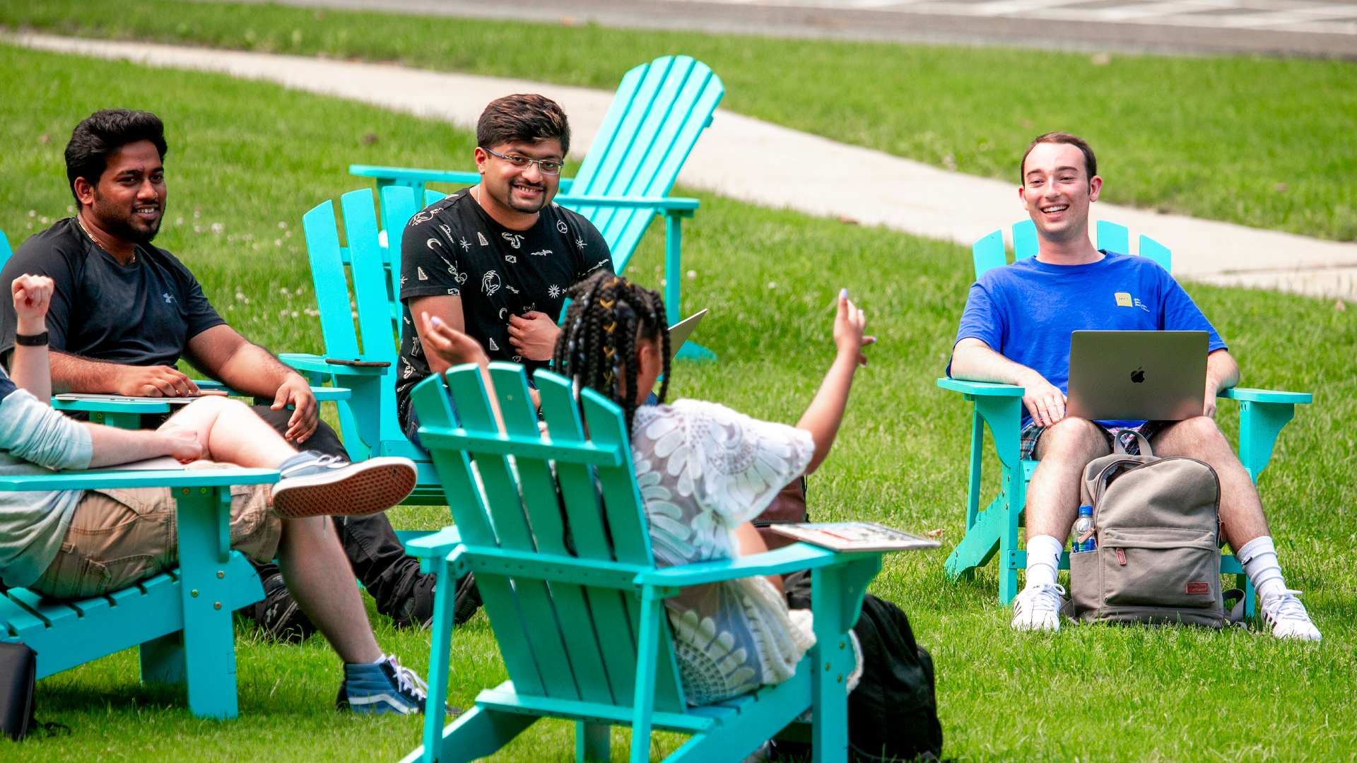 A group of student lounge on brightly colors Adirondack chairs on campus.