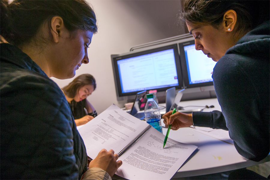 Two students looking over notes with computer screens in the background.