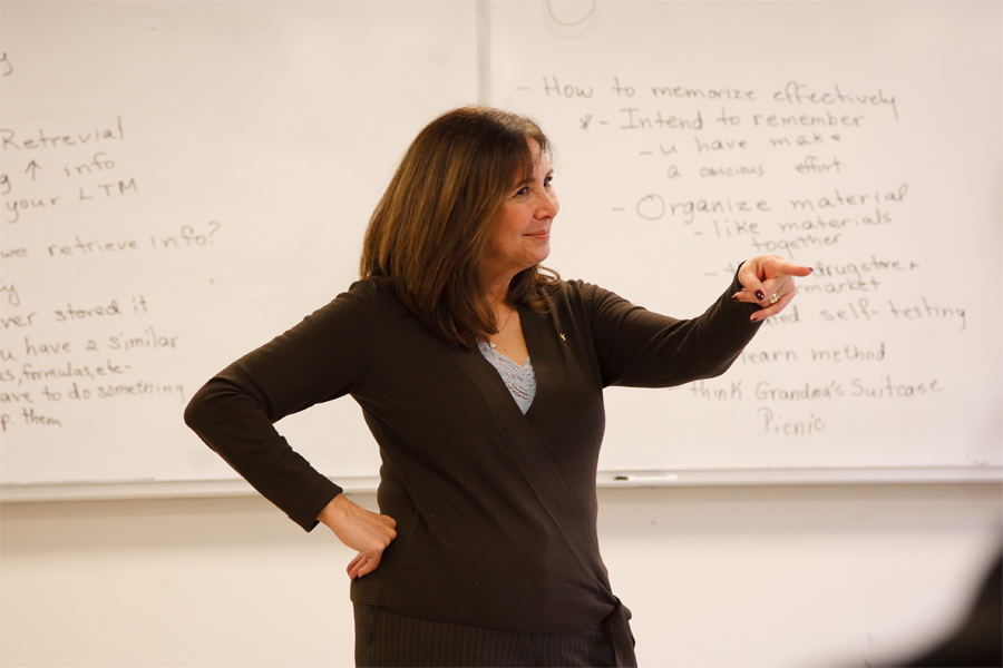 A faculty member standing in front of a whiteboard smiling and pointing at a student. 