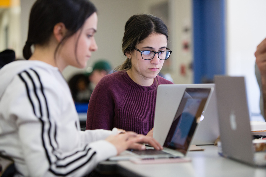 Two students studying a table in a student lounge with their laptops.