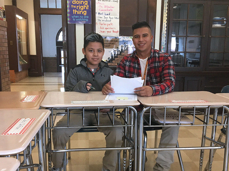 Fabian Escobedo (M.S. '18) sits in a school classroom in front of one of his students. 