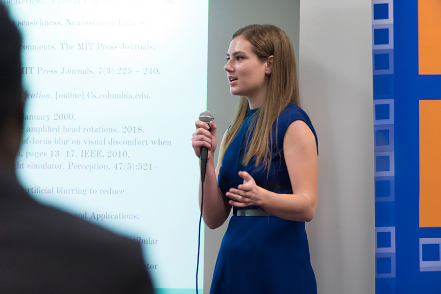 A student presenting in front of a projection holding a microphone.