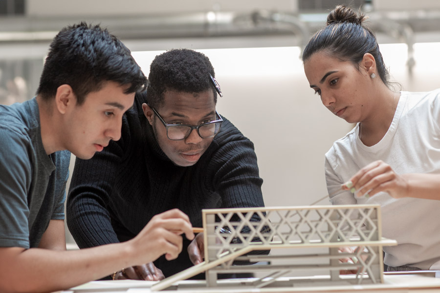 Three students in New York Tech's Department of Architecture discuss a 3-D model structure with lattice elements.