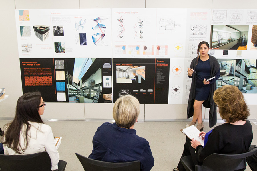 Standing in front of multiple poster boards, a student enrolled in New York Tech's Department of Interior Design presents her ideas to an audience of faculty members.