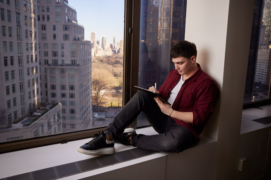 Sitting near a window, a School of Architecture and Design graduate student attending New York Tech's New York City campus draws on a tablet.