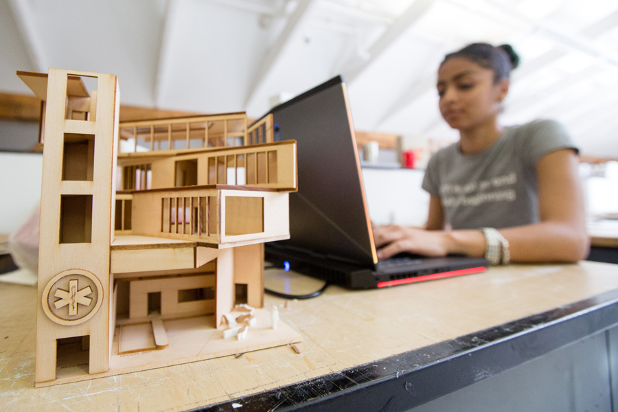 A student works on a laptop on a table with a model of a building.