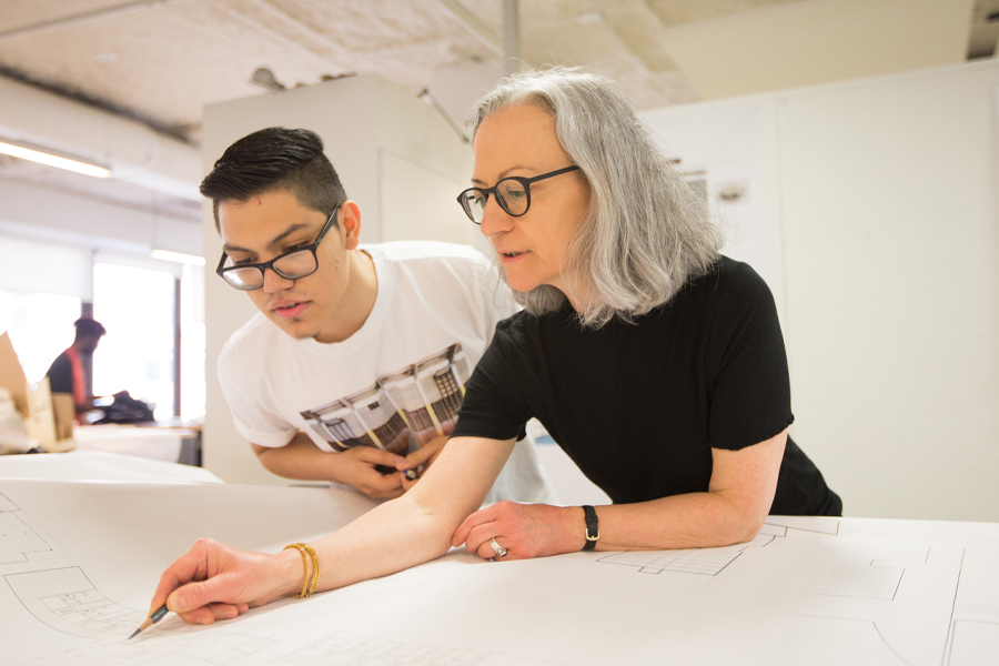 A faculty member is reviewing a blueprint with a student in a classroom.