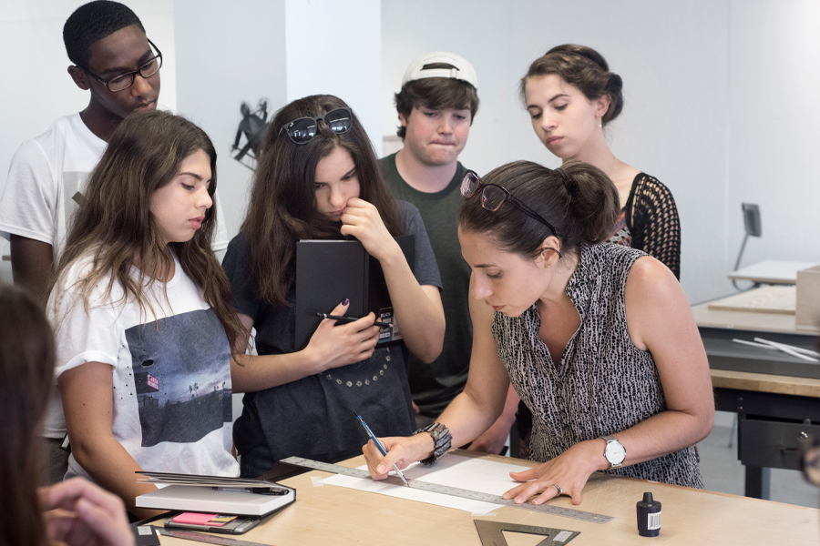 A group of students watch as an instructor draws out plans for a project.