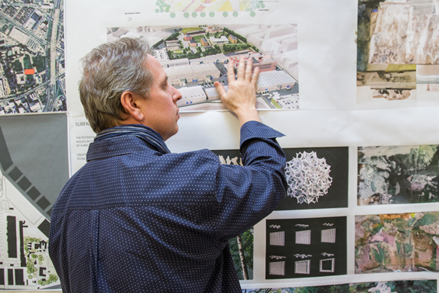 A faculty member reviewing drawings on a wall. 