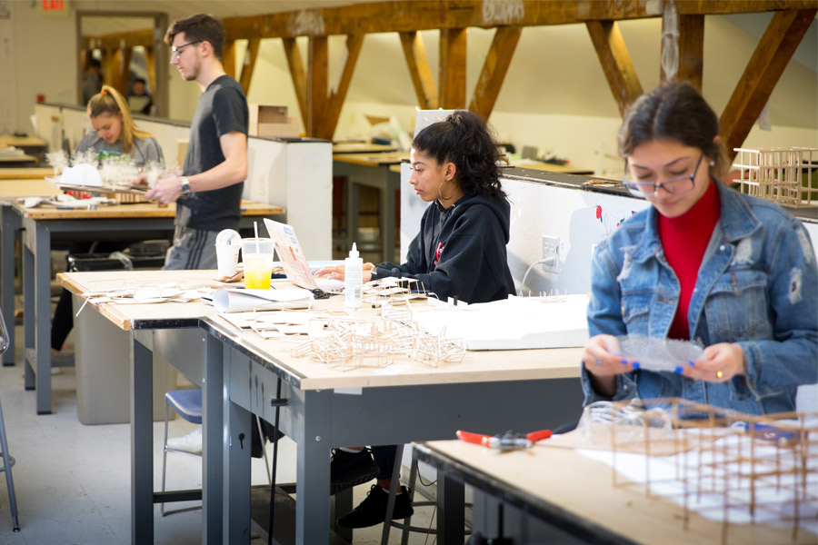 Four students work on their individual projects in a design workshop.