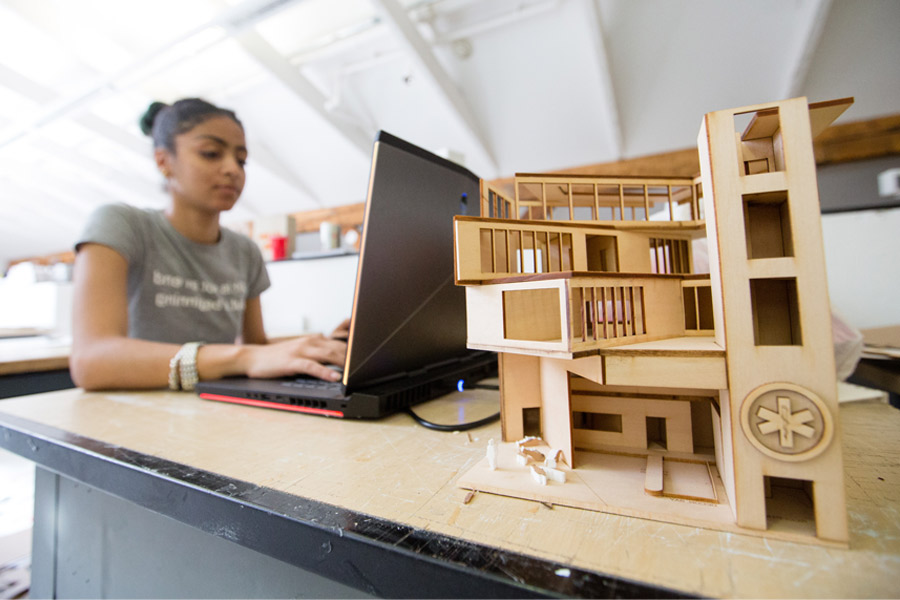 A student works on a laptop on a table with a model of a building.