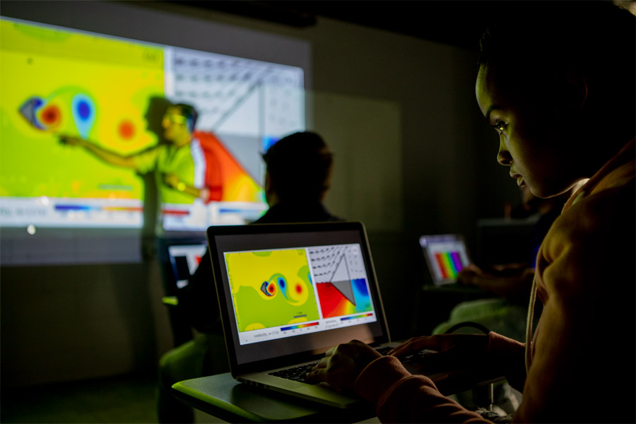 As an instructor traces a topographical map on a screen, a New York Tech mathematics student studies a related problem on their laptop.