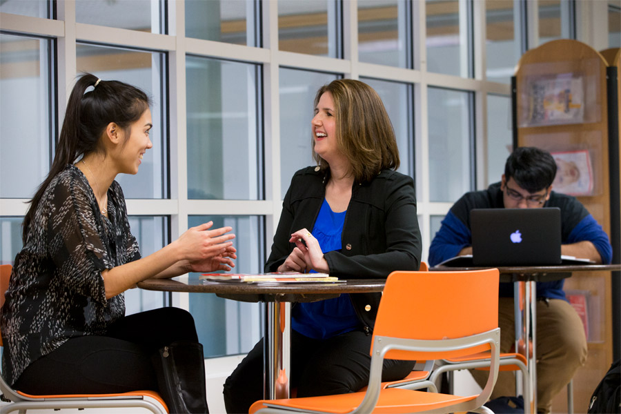 Two students from New York Tech's Department of Psychology and Counseling engage in conversation at a table in one of the school's common areas.