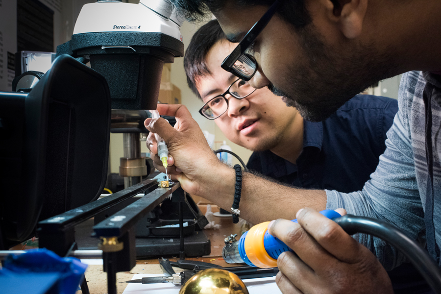 Two students work on a circuit board adding flux and holding a soldering iron. 