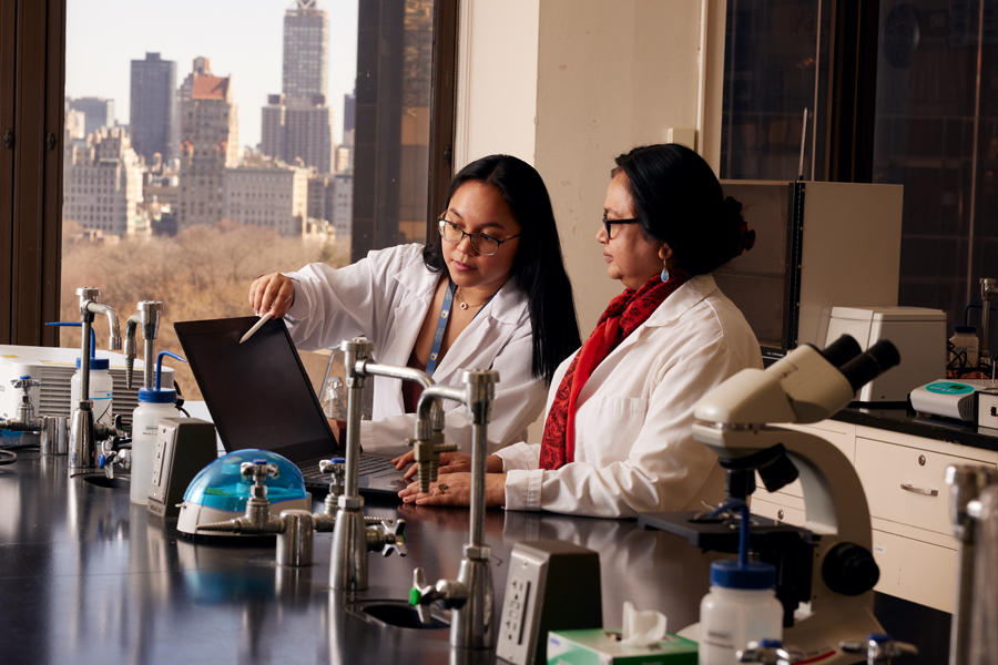 A faculty member and a student in lab coats working on a project together in a lab.