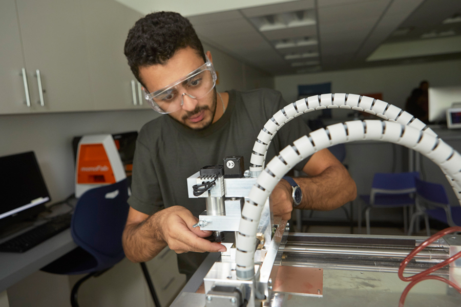 A student is working with a fabrication machine in a lab. 