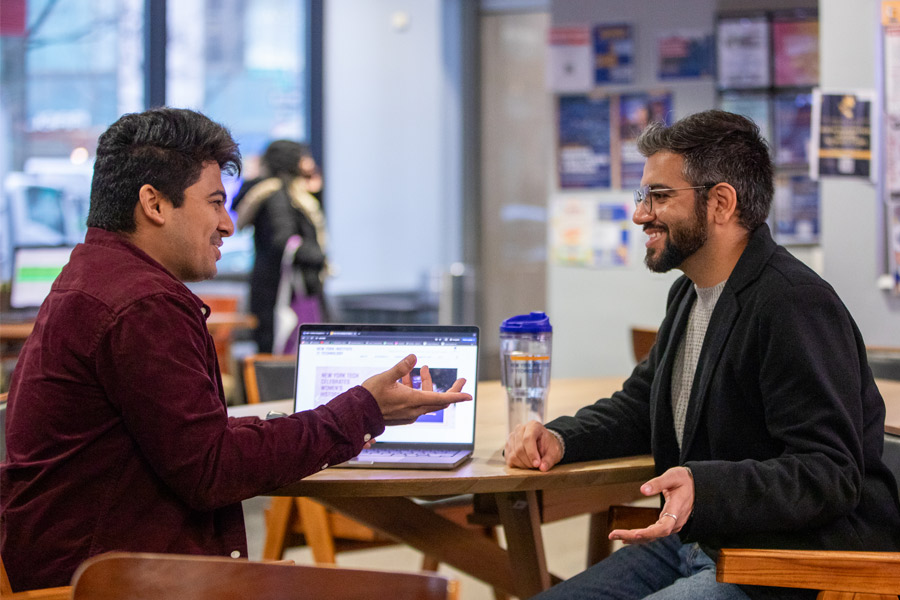 Two people sitting at a table in student lounge on the New York Tech NYC campus.