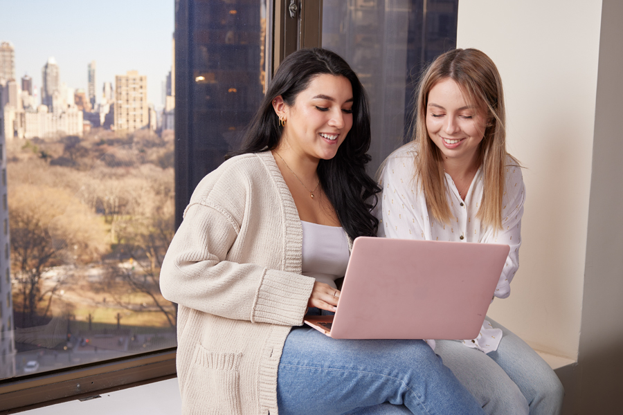 Two students studying by a window with laptop.