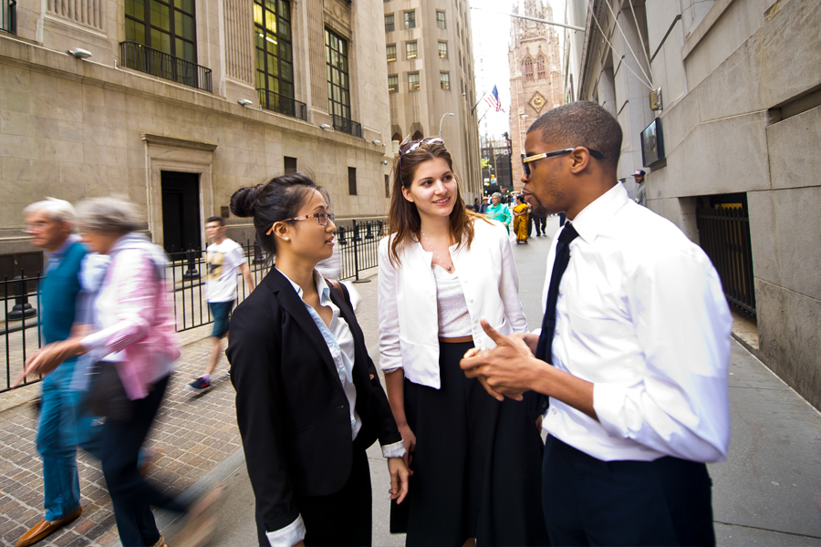 Three students in business attire on city sidewalk.