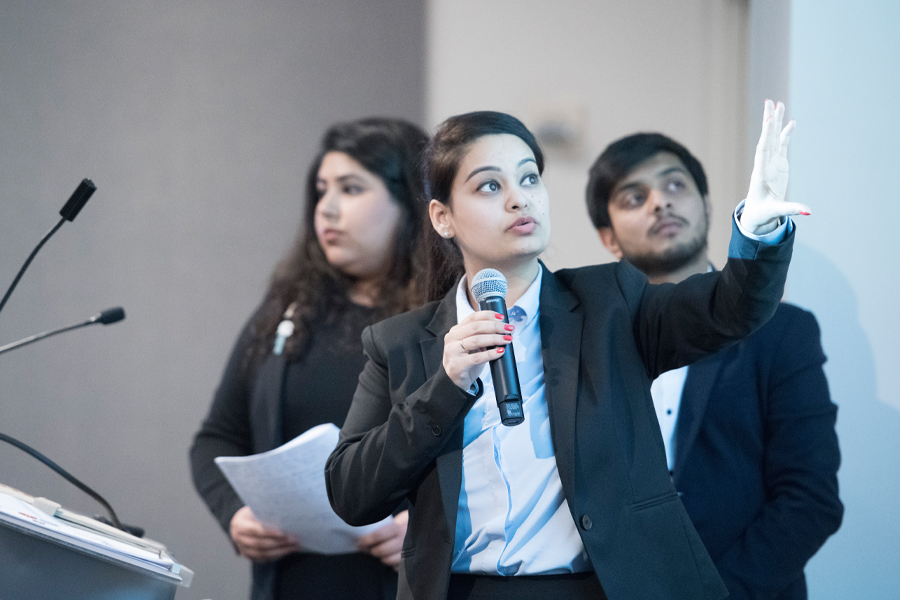 Three students presenting in auditorium.