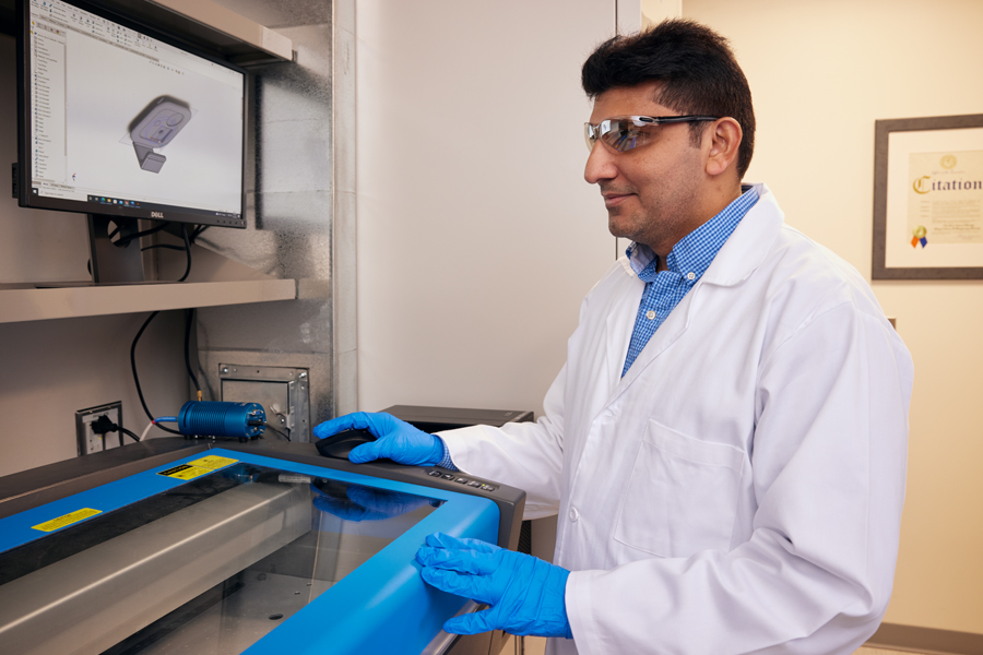 A faculty member wearing a white lab coat and protective gear conducting research in a lab. 