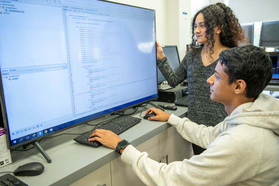 Two students in front a large screen in lab. 