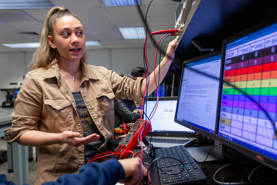 A student in a lab with electrical equipment and a computer showing readings. 