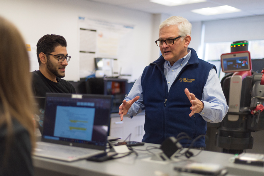 President Hank Foley speaking with students in a robotics lab on campus.